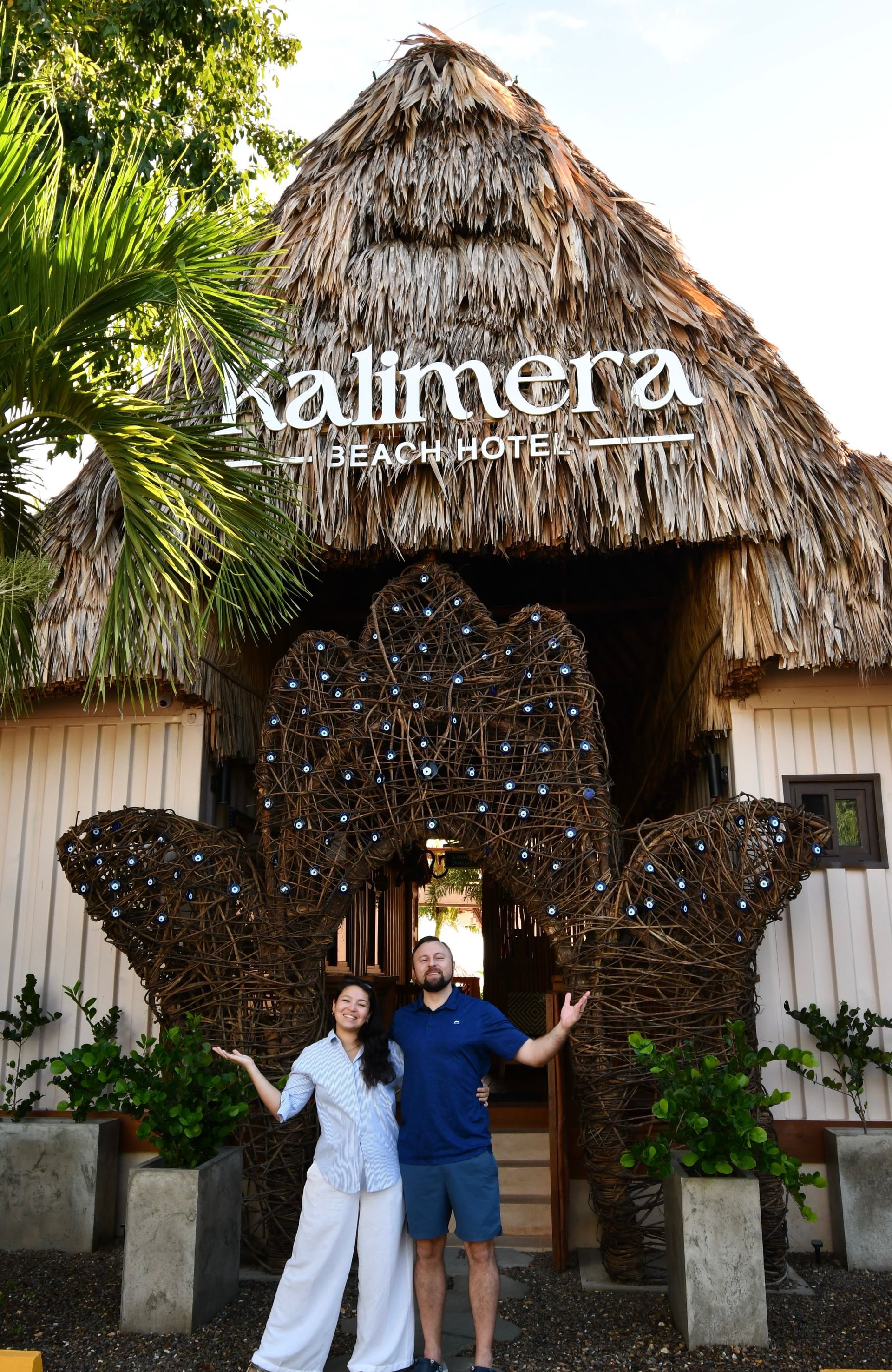 A man and a woman are standing in front of a building that says kalimera