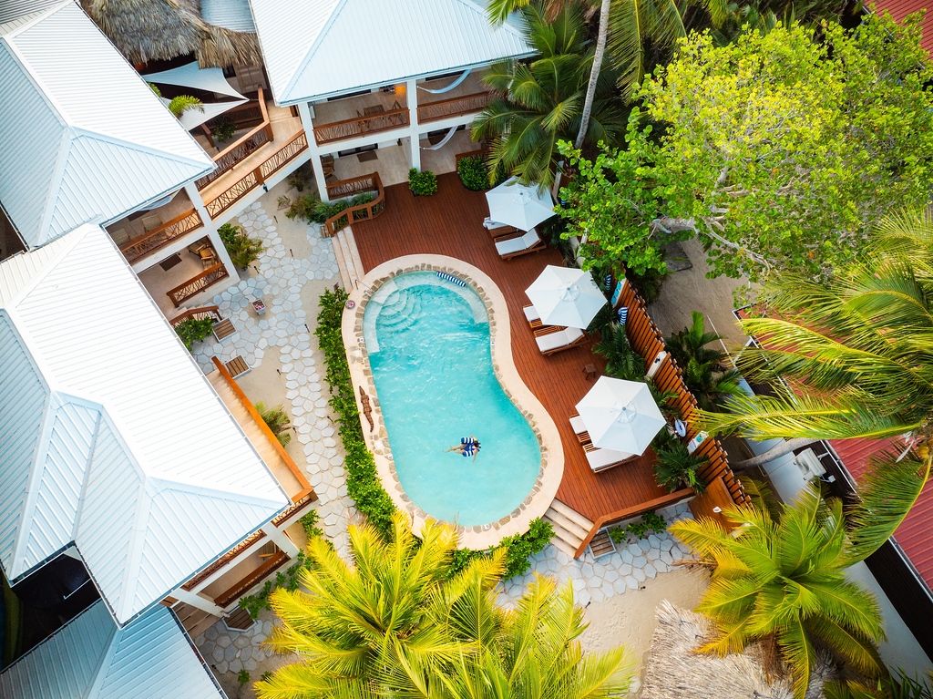 Aerial view of a resort with a pool, white buildings, and tropical greenery.