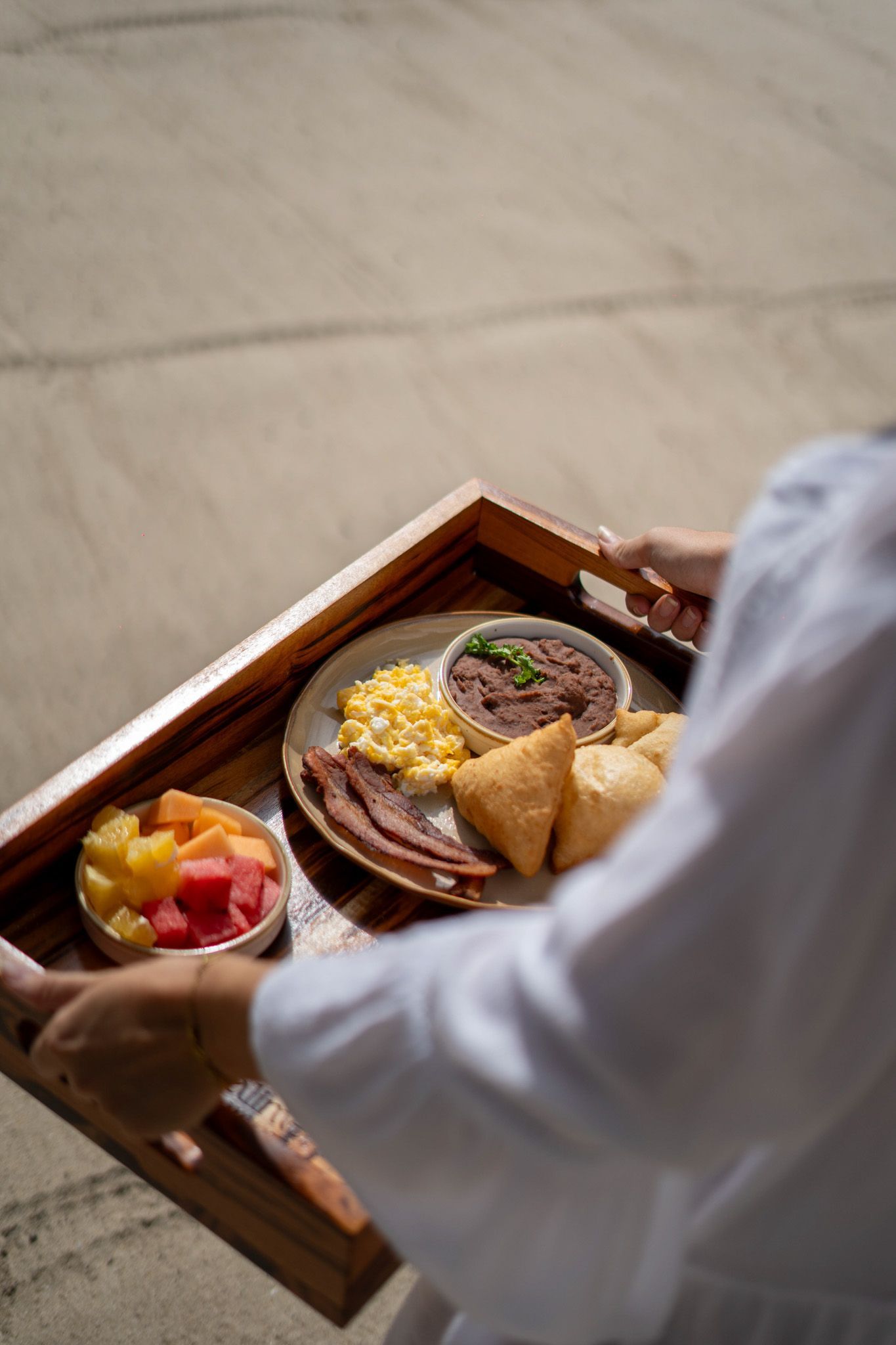 A person is holding a wooden tray with food on it.
