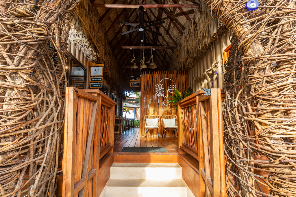 Entrance of a tropical-style hut, with a woven thatch archway and wooden railings.