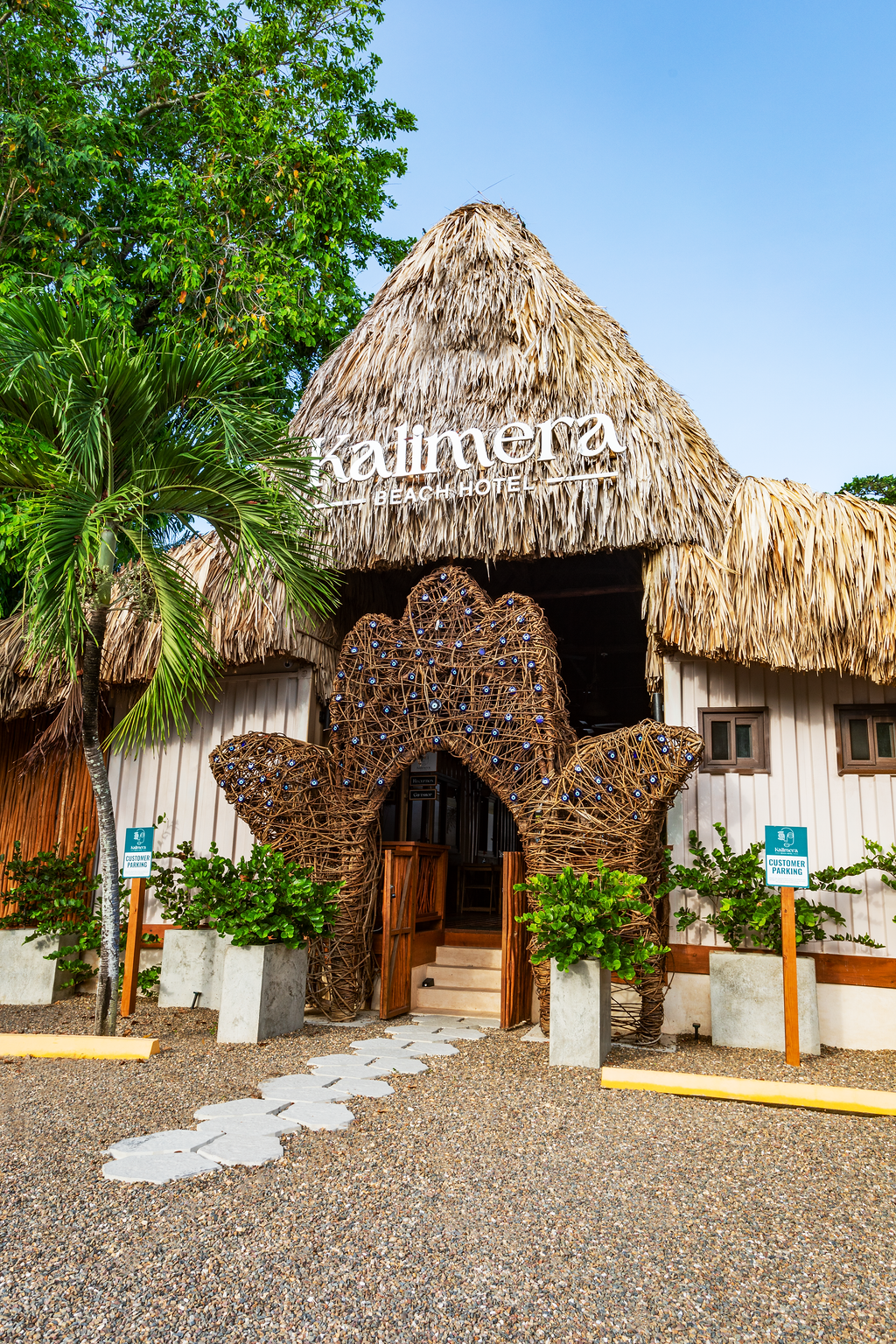 Kailmey restaurant with thatched roof, decorative wooden entry, plants, and parking signs.