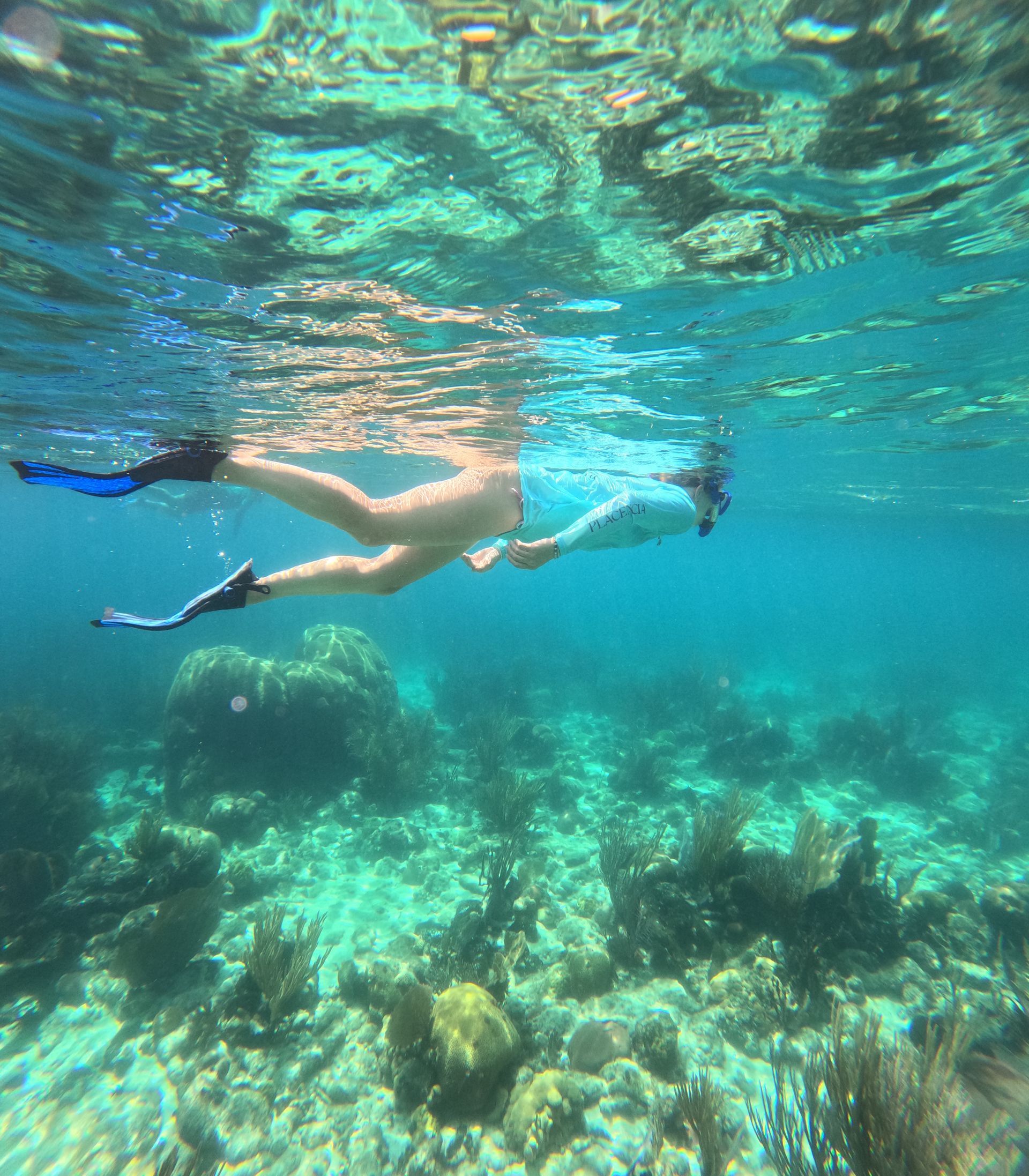 Person snorkeling above a coral reef in turquoise water.