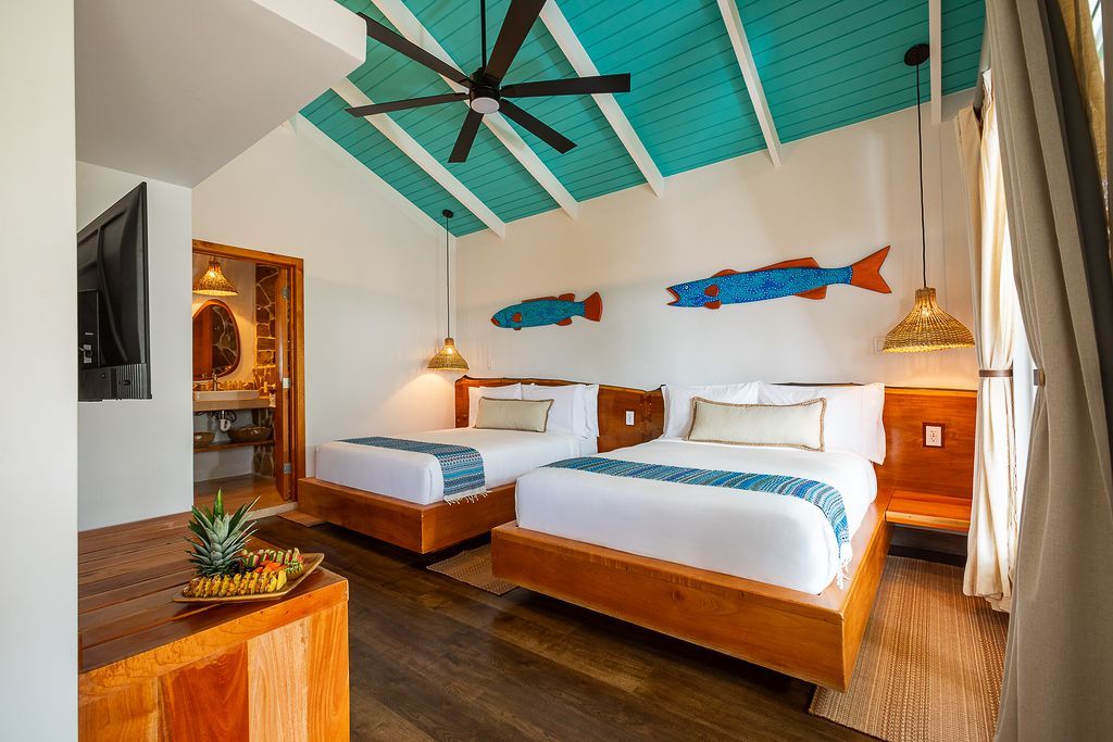 Bedroom with2 double beds , blue shark art, and balcony access with lush greenery.