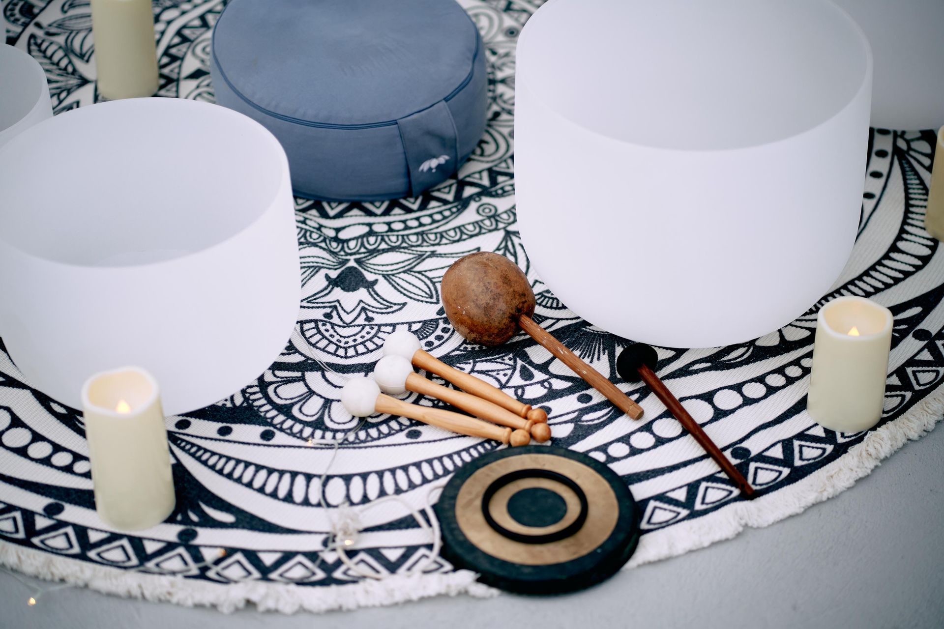 Crystal singing bowls, meditation cushions, mallets, and candles on patterned rug.