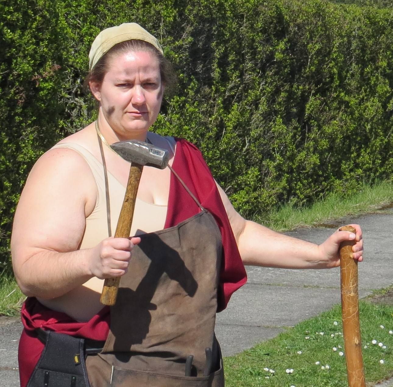 A woman is holding a hammer and a cane, representing Hephaestus.