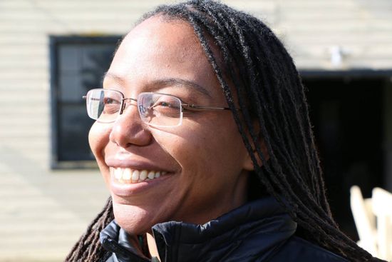 A woman wearing glasses and dreadlocks is smiling