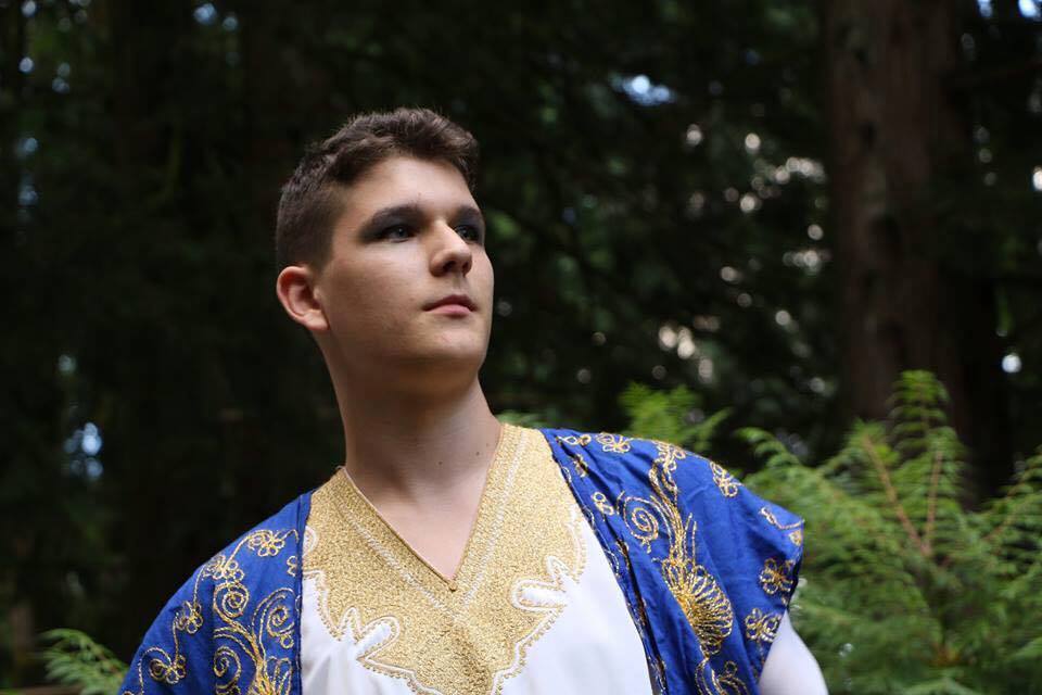 A young man in a blue and gold costume is standing in the woods.