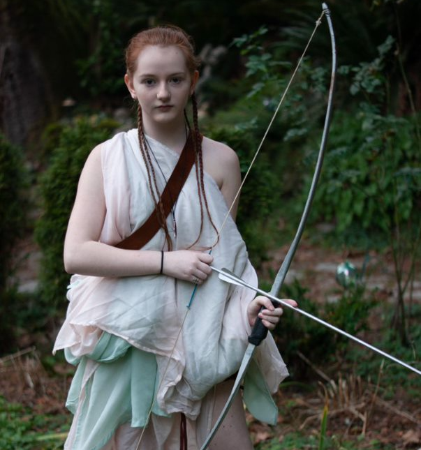 A woman in white holding a bow and arrow