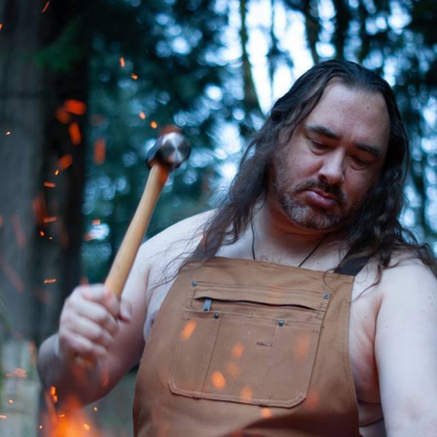 A shirtless man in an apron is holding a hammer, representing Hephaestus.