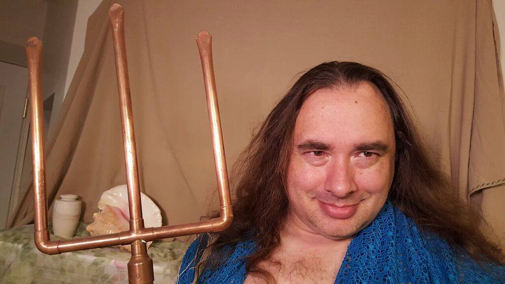 A man with long hair is holding a copper fork, representing Poseidon.