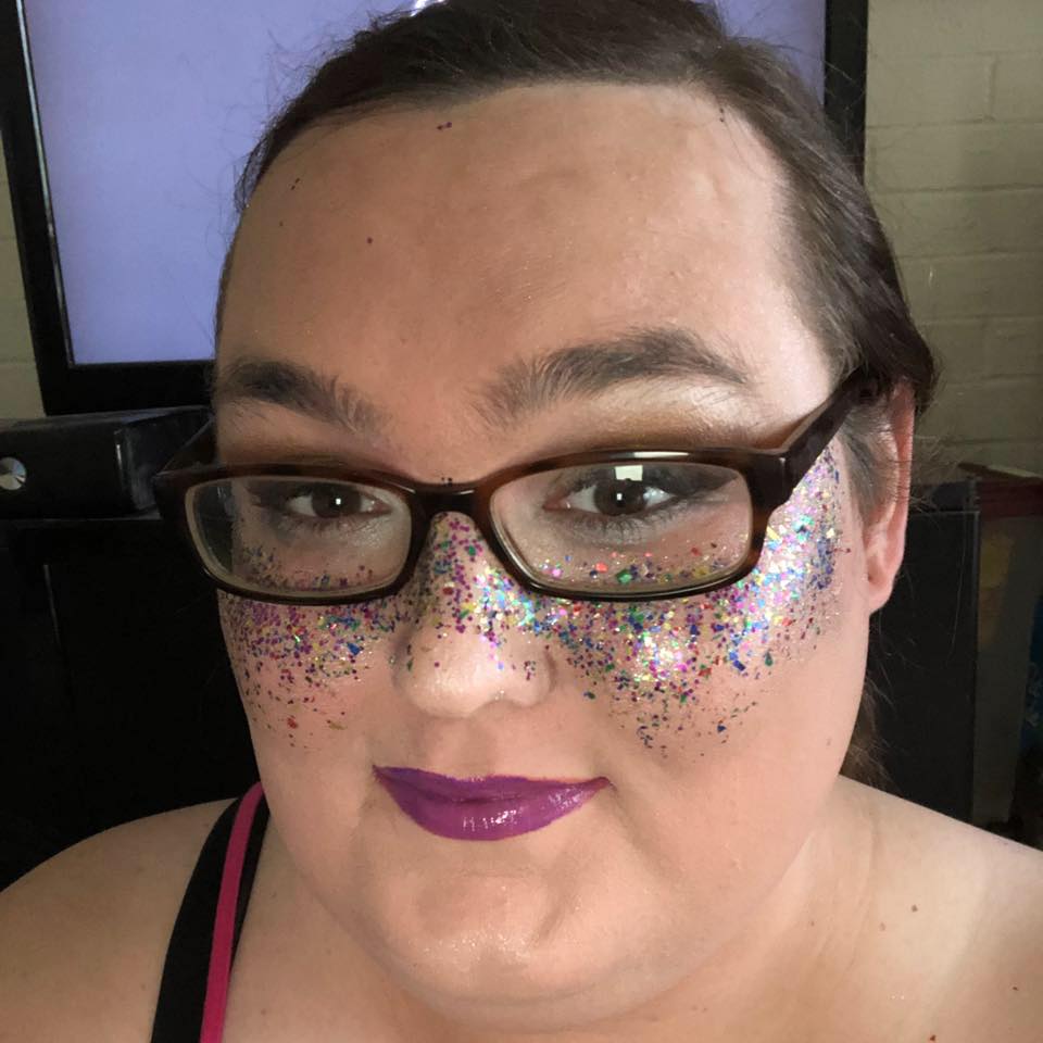 A woman wearing glasses and glitter on her face, Ella Hayes.