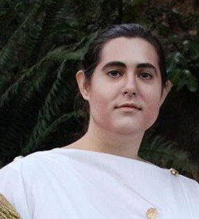 A woman in a white dress is standing in front of a tree.