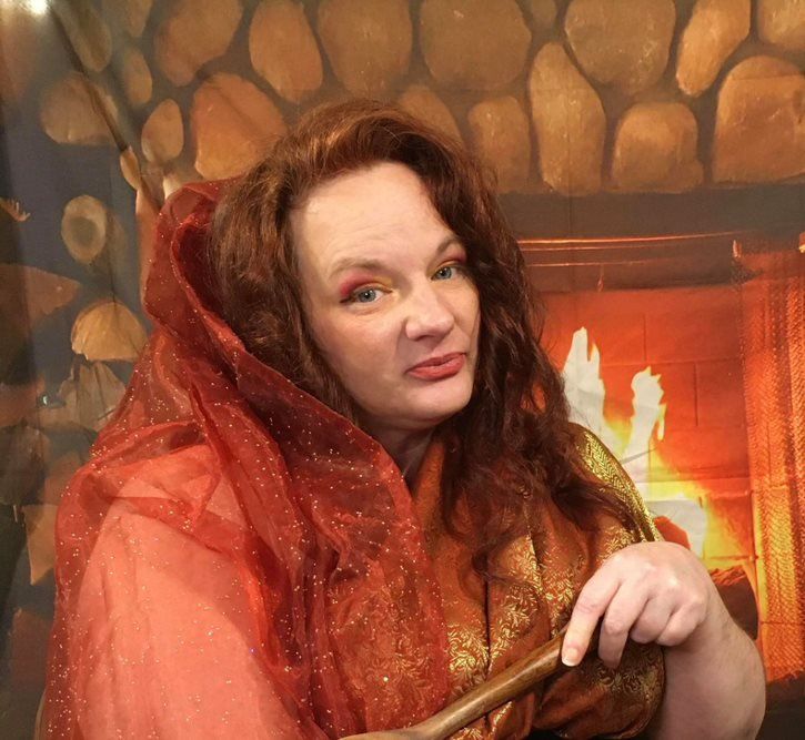 A woman is holding a wand in front of a fireplace, Isidora LaVeau representing Hestia.