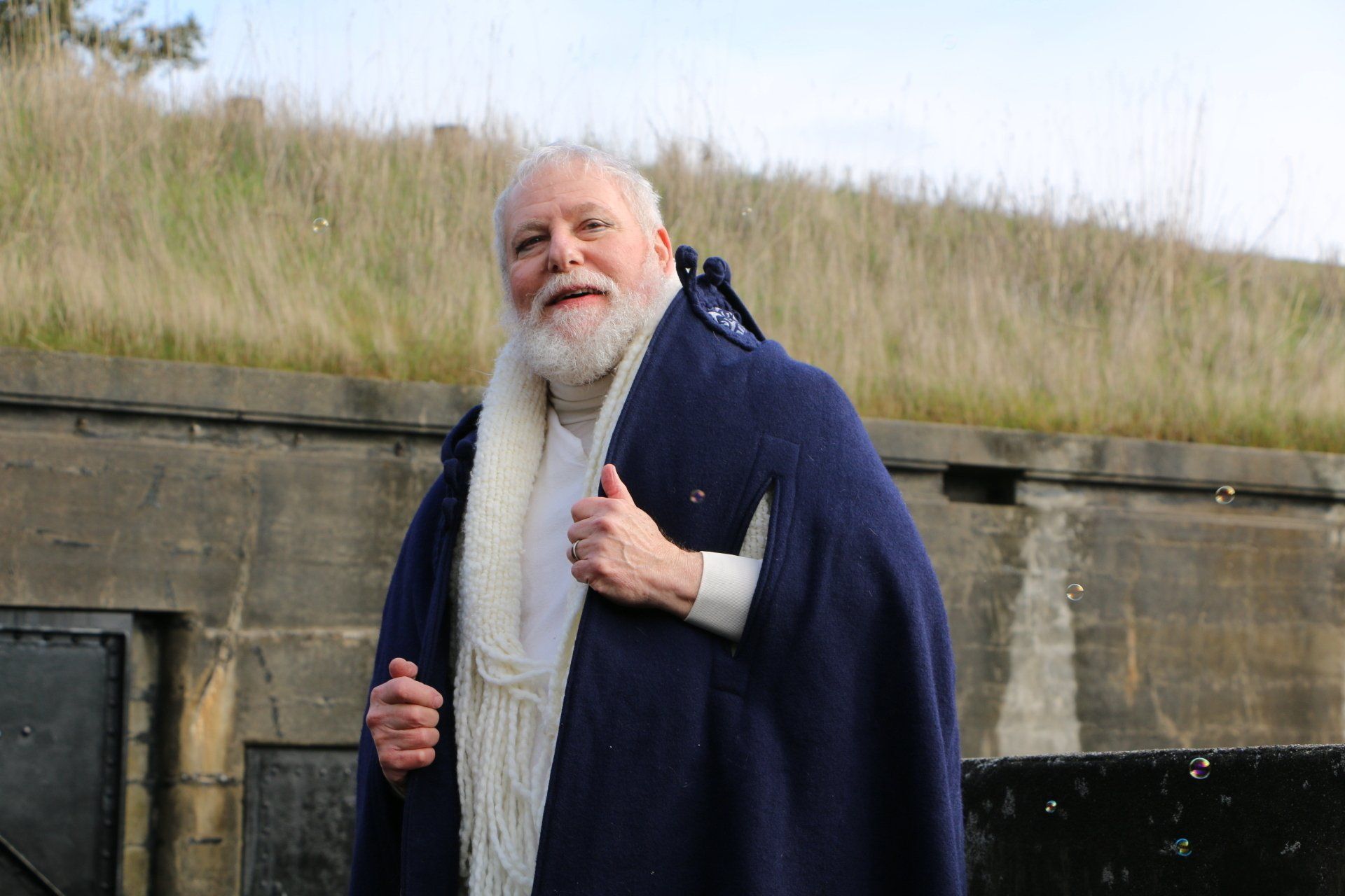 A man with a beard is wrapped in a blue blanket and giving a thumbs up.
