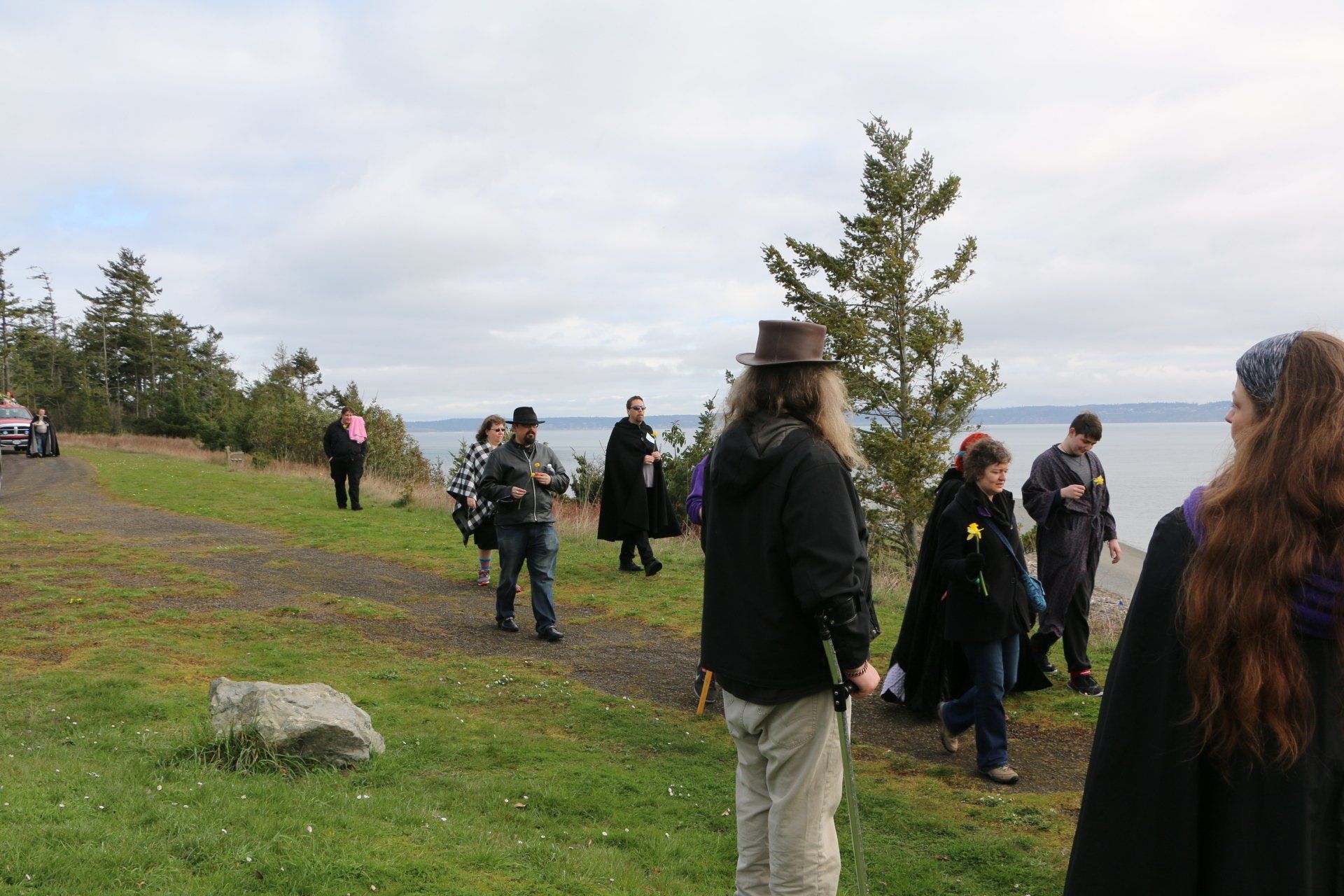 A group of people are standing on a grassy hill near a body of water.