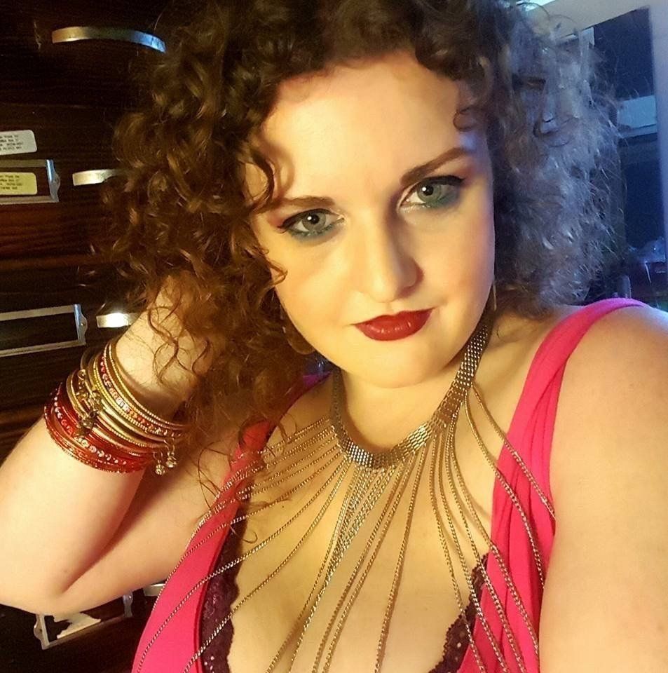 A woman with curly hair is wearing a necklace and bracelets