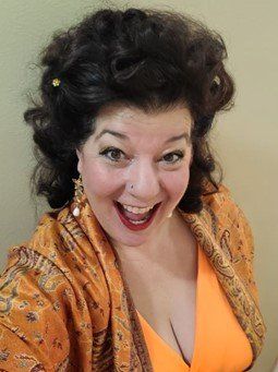 A woman wearing an orange top and a scarf is smiling representing Baubo.