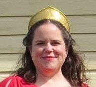 A woman wearing a red dress and a gold crown is smiling, representing Hestia.