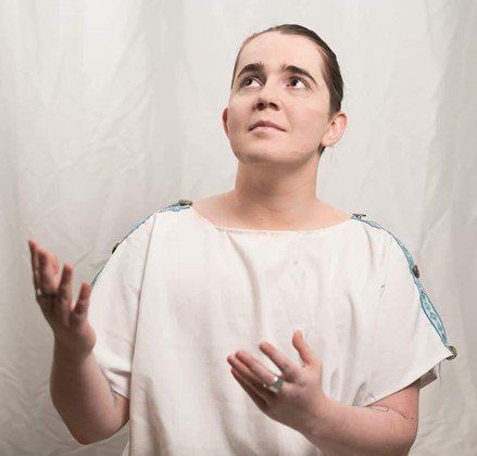 A woman in a white shirt is looking up at the sky, representing Eumolpus.