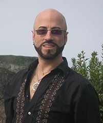 A bald man with a beard is wearing sunglasses and a black shirt.