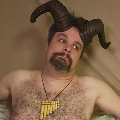A shirtless man with a beard and horns is wearing a necklace, representing Pan.