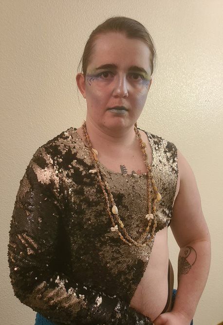 A woman is wearing a sequined top and a gold necklace, representing Poseidon.