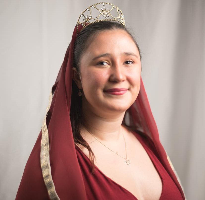 A woman wearing a red dress and a tiara is smiling, Raven Wolfenone representing Hestia.