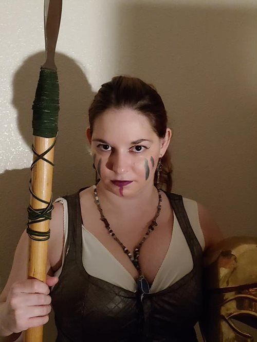 A woman is holding a wooden pole with a green rope around it, Titania Thunderlily representing Athena.