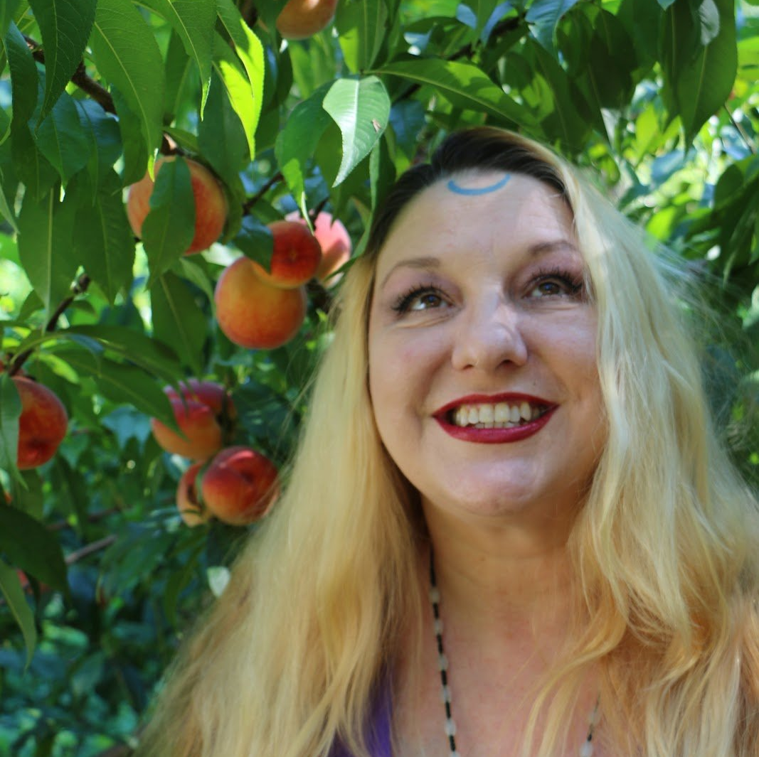 A woman is smiling in front of a peach tree, Belladonna LaVeau.