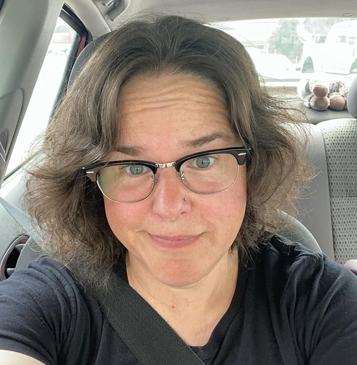 A woman wearing glasses is taking a selfie in the back seat of a car, Joy Mainer.