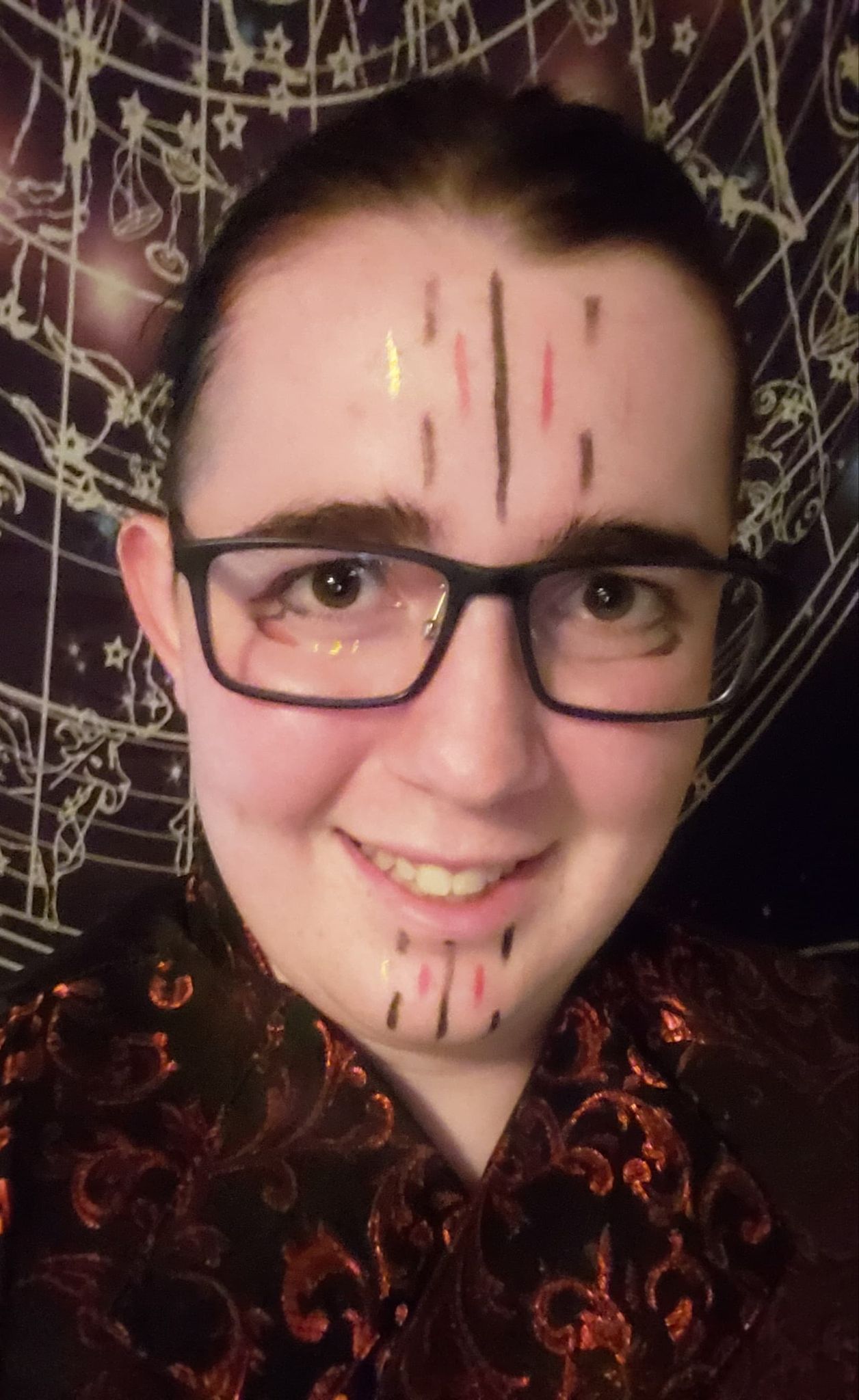 A young man with glasses and a tattoo on his face is smiling.