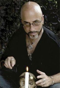 A man is sitting in front of a skull and a candle.