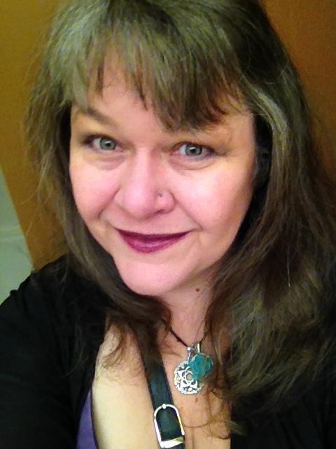 A woman with long hair and a necklace is smiling for the camera.