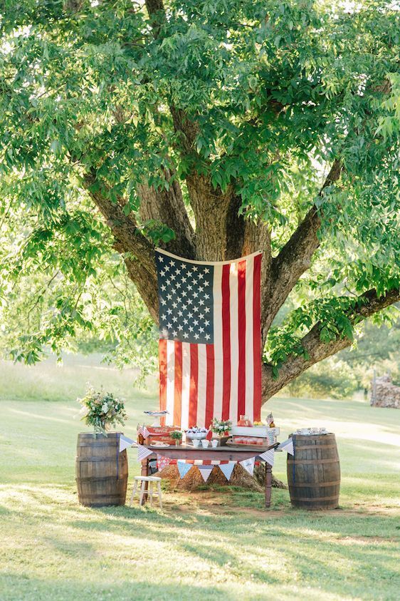 a large american flag is hanging from a tree next to a table .