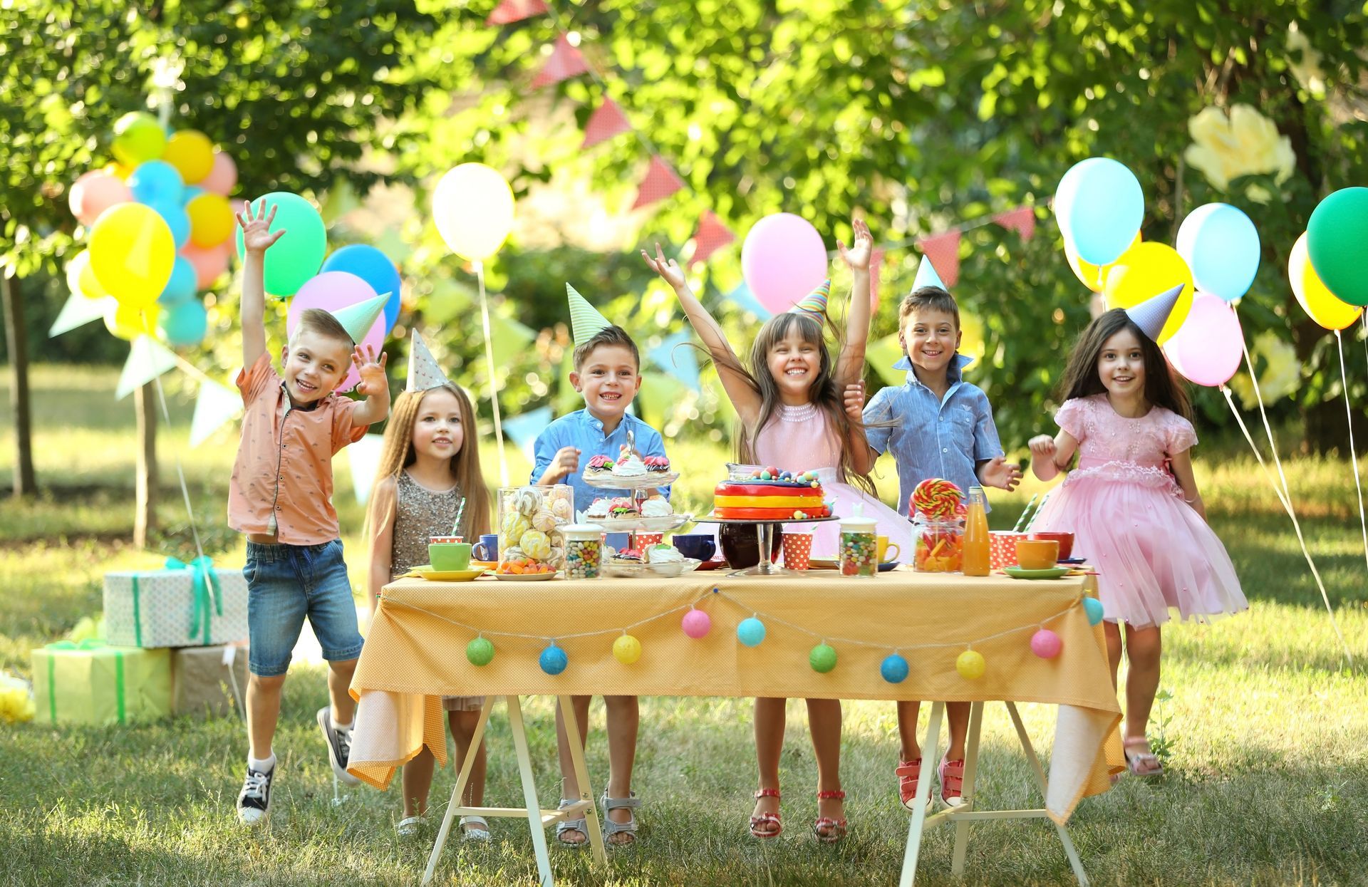 a group of children are standing around a table with balloons at a birthday party .