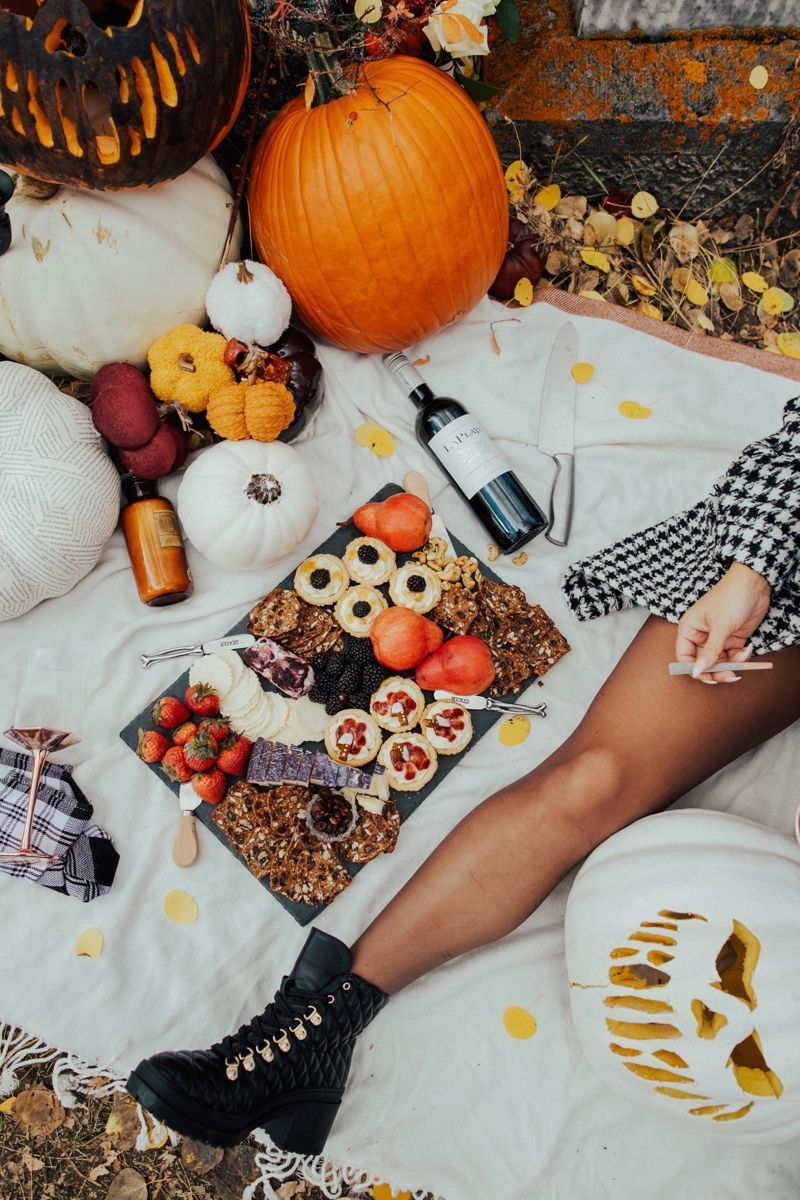 a woman is laying on a blanket surrounded by pumpkins and food .