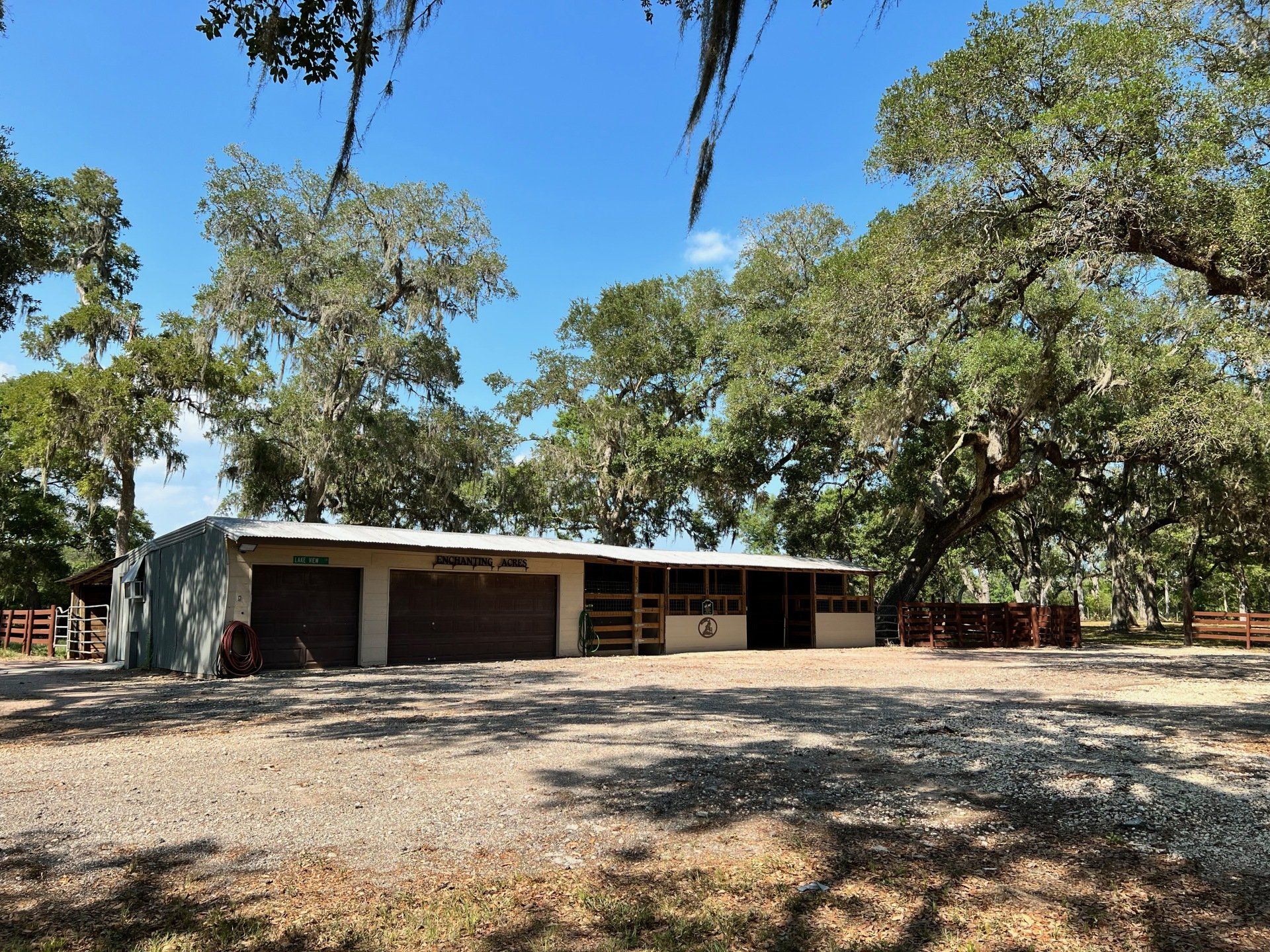 a horse stable is surrounded by trees on a dirt road .