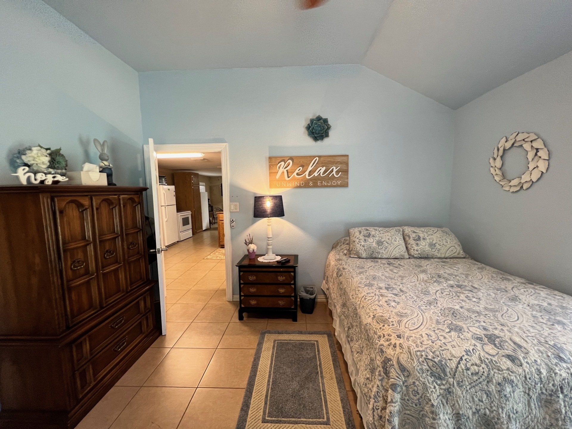 a bedroom with a bed , dresser , nightstand and a sign on the wall that says `` relax '' .