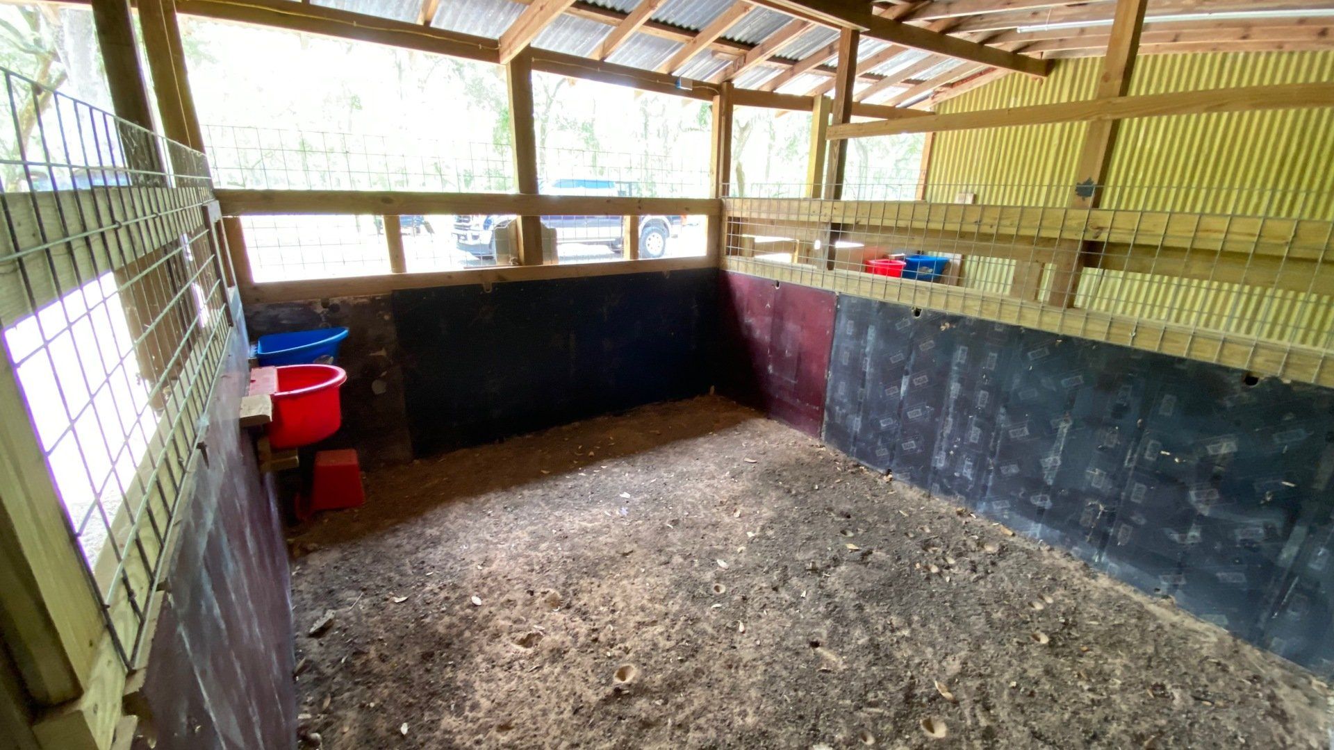 an empty horse stable with a fence and buckets in it .