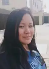 a woman with long black hair is standing in front of a building and smiling .