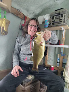 a woman is sitting on a cooler holding a fish .