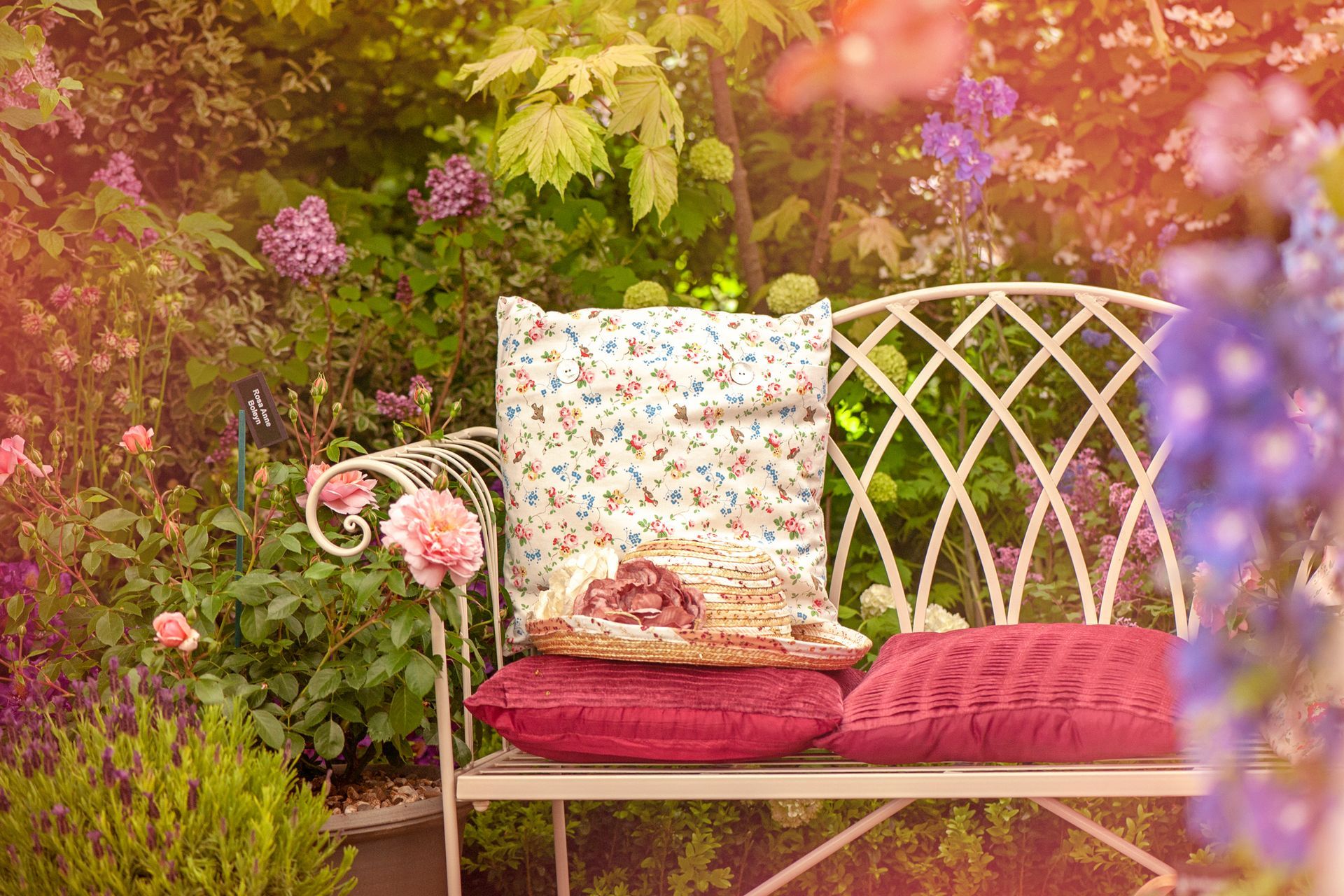 A bench with pillows on it in a garden surrounded by flowers.