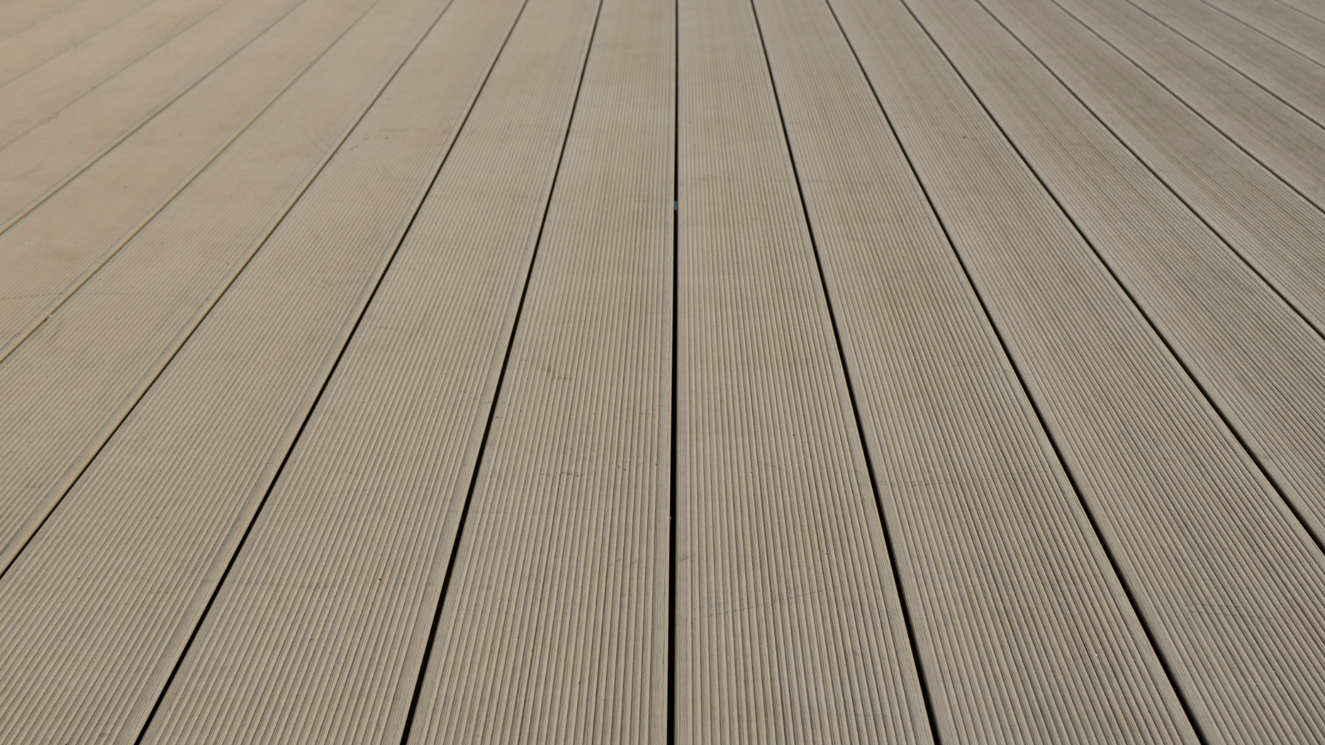 An angled, close-up perspective of parallel light brown composite decking planks with a textured wood grain pattern.