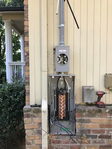 Electrical service box mounted on a brick wall with conduit leading upwards.