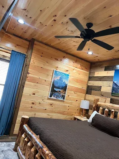 Bedroom with log bed, wood paneling, artwork of mountains, and a ceiling fan.