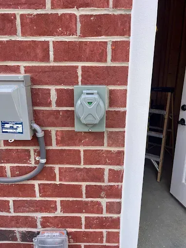 Gray electrical outlet on red brick wall, next to a metal box and a white door.