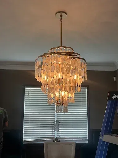Ornate, layered chandelier with shell-like discs hanging over a dining table.