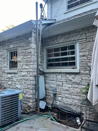 Stone building exterior with windows, air conditioning unit, and metal utility pipes.