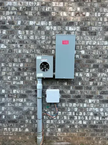 Electrical equipment mounted on a gray brick wall: meter box, gray panel, and a smaller white box.