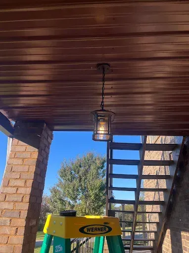 Outdoor light fixture hanging from a brown metal ceiling. A ladder is in the foreground.